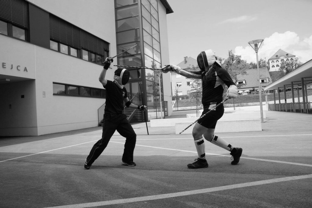 Two club members sparring with one stick in each hand, in advanced gear.