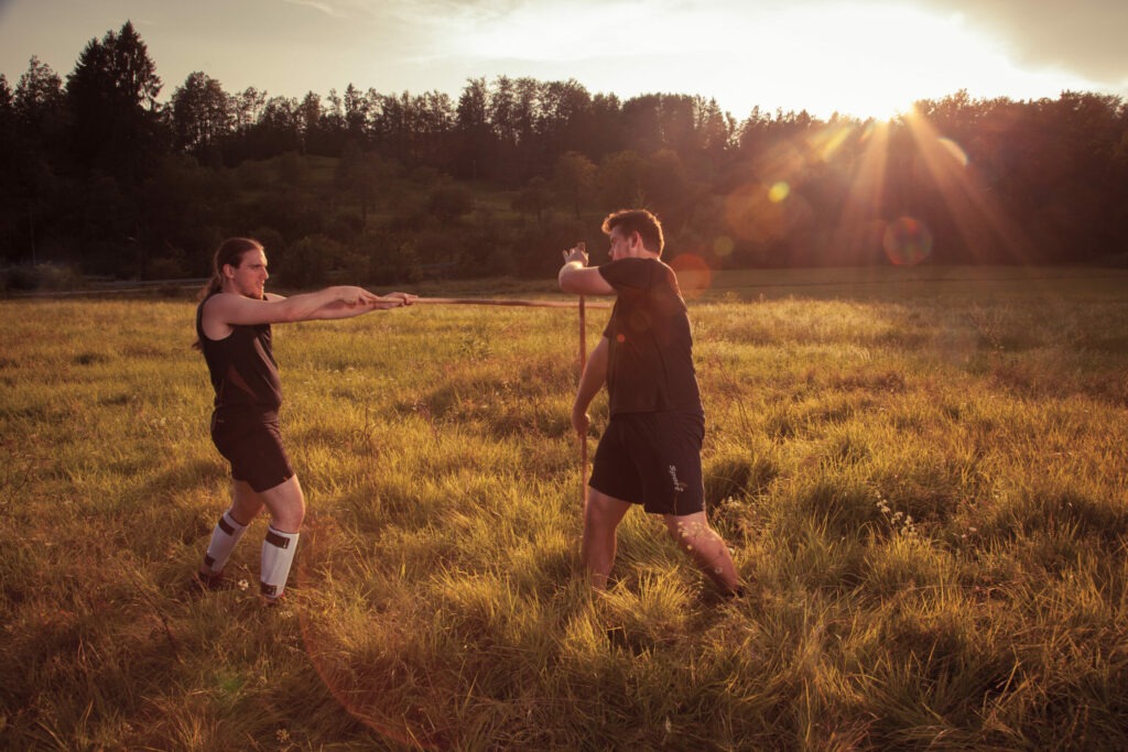 Two men sparring with bâton in a field